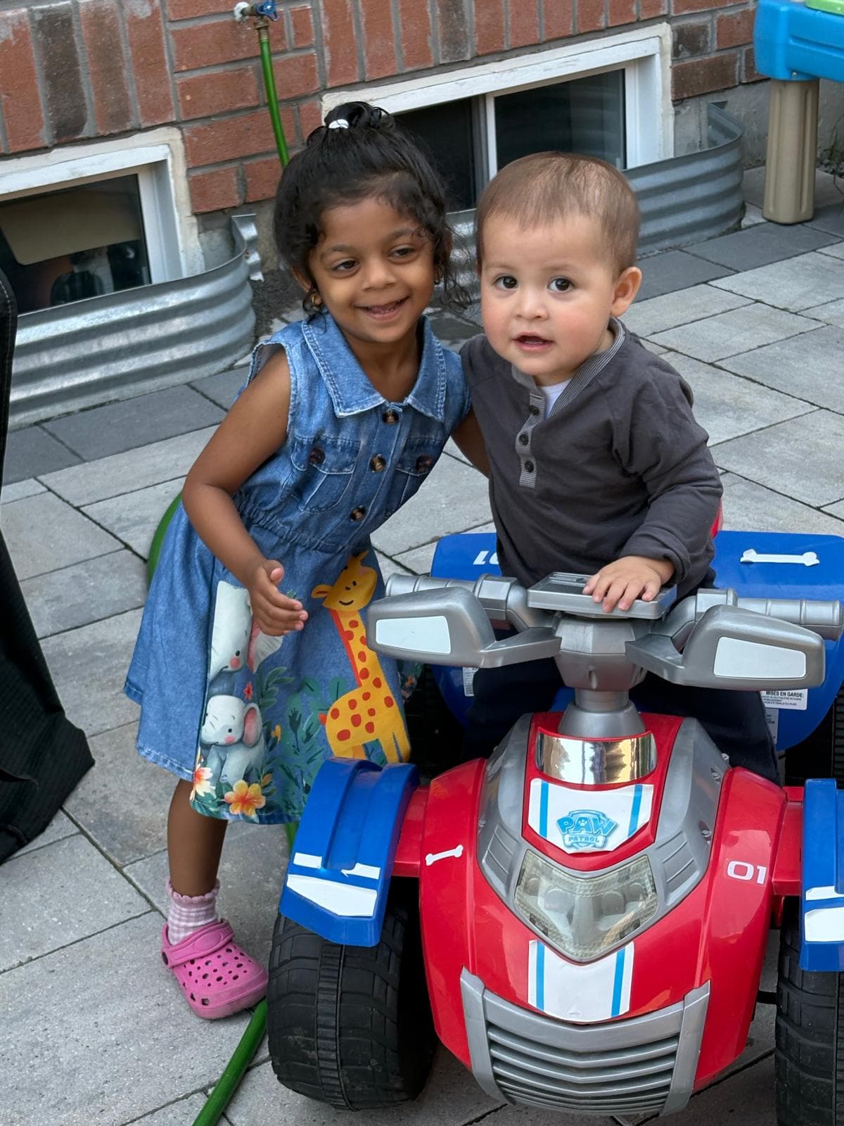 2 kids hugging and smiling for the camera on top of a toy car