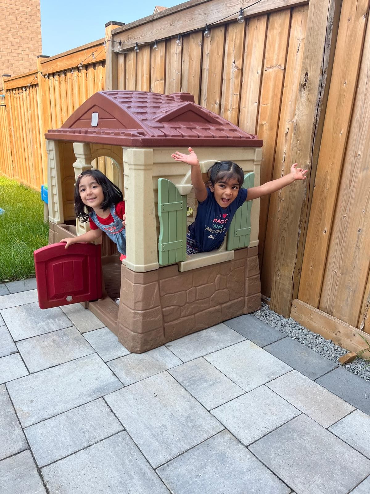 2 kids peaking through the windows of outdoor mini house